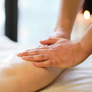 Hands massaging a person's leg on a massage table with a lit candle in the background.