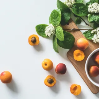 Apricots and leaves on a wooden board with a white bowl.