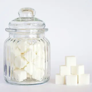 Glass jar filled with sugar cubes, next to a stack of sugar cubes on a white background.