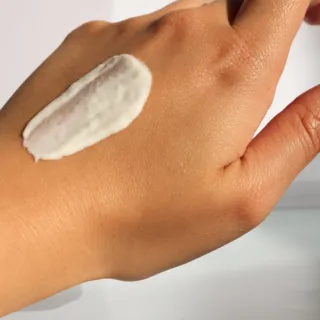 Cream applied on the back of a hand against a light background.