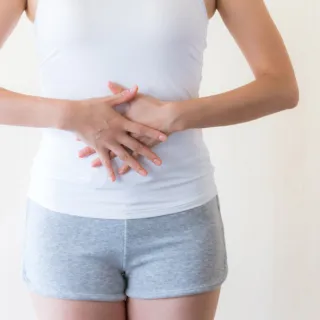 Person in white top and grey shorts holding stomach with both hands.