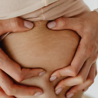 Hands pressing skin on a person's abdomen.