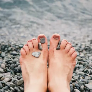 Bare feet on pebbles by the sea, small stones on toes.