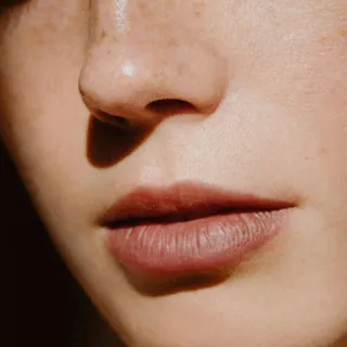 Close-up of a person's nose and lips with freckles and smooth skin.