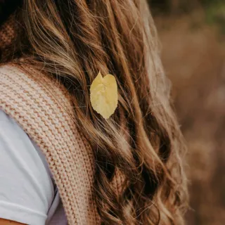 Curly hair with a yellow leaf, wearing a knitted beige scarf.