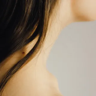 Long dark hair and a mole on a woman's neck against a neutral background.