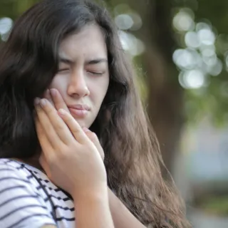Woman with long hair touching her cheek, eyes closed, outdoors.