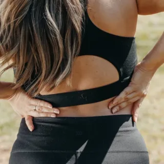 Woman in black sportswear holding her lower back outdoors.