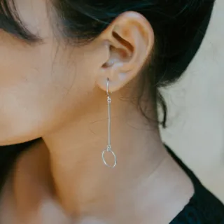 Silver drop earring with circular pendant worn by a person with dark hair.