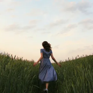 Woman in a striped dress walking through a grassy field at sunset.