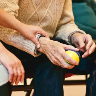 Person holding an elderly person's hand, who is holding a yellow and blue ball.