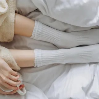 Person in cosy socks and robe holding a mug on a white bed.