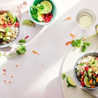 Two bowls of salad with avocado, lime, and herbs on a light table setting.