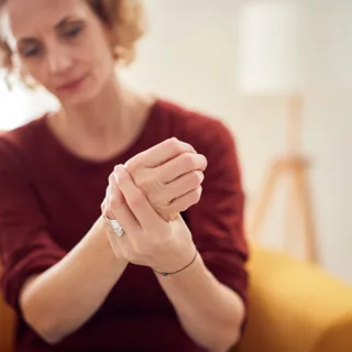 Woman in red jumper massaging her hand on a yellow sofa.