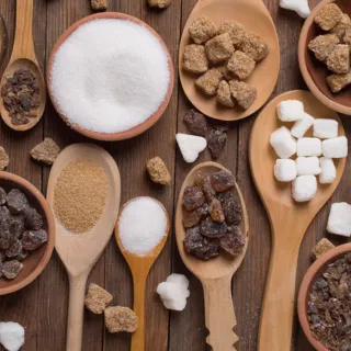 Various types of sugar in bowls and spoons on a wooden surface.