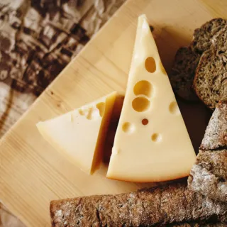 Cheese slices with holes on a wooden board, surrounded by brown bread slices.