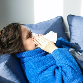Person in blue jumper using tissue on sofa.