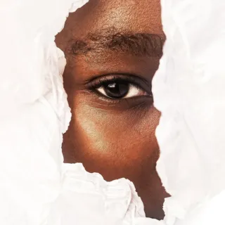 Eye peering through torn white paper.