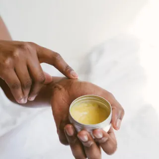 Hand applying balm from a small tin container.