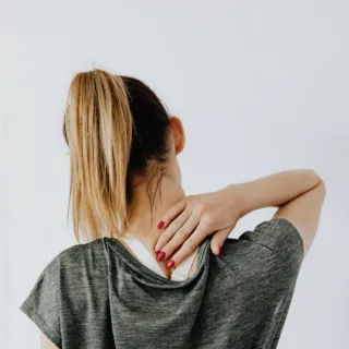 Person with ponytail touching neck, wearing grey top.