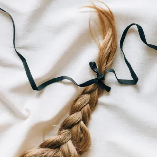 Braided hair tied with a black ribbon on a white fabric background.
