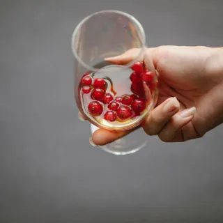 Hand holding a glass with red berries and liquid inside.