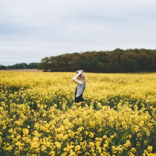 Person standing in a field of yellow flowers under a cloudy sky.