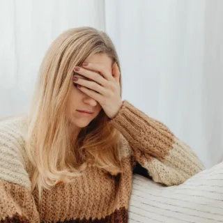 Woman in a striped jumper covering her face with her hand, sitting on a sofa.