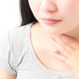 Woman touching her throat with one hand, wearing a grey top.
