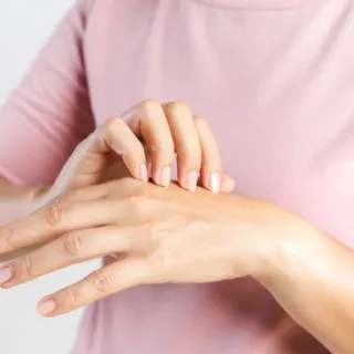 Person applying cream to the back of their hand, wearing a pink top.