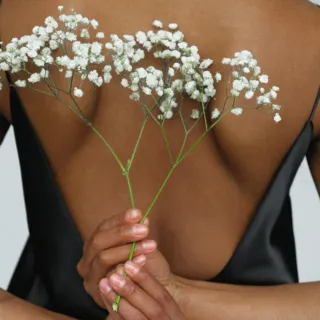 Person in black dress holding white flowers behind back.