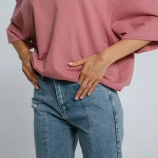 Person wearing a pink top and blue jeans, hands on hips, against a plain background.