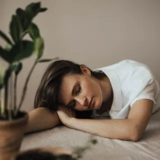 Woman resting on table near potted plants indoors.