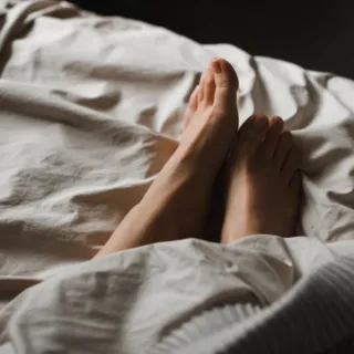 Feet under white bed sheets in dim lighting.