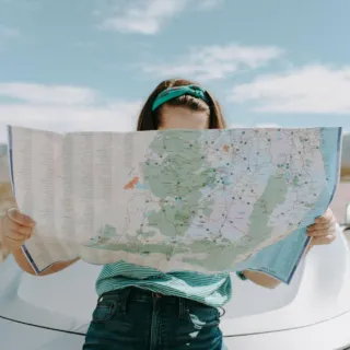 Person reading a large map while leaning on a car in a desert landscape.