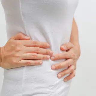 Person in white shirt holding their side with both hands.