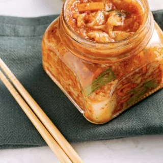Jar of kimchi on a green cloth with wooden chopsticks beside it.