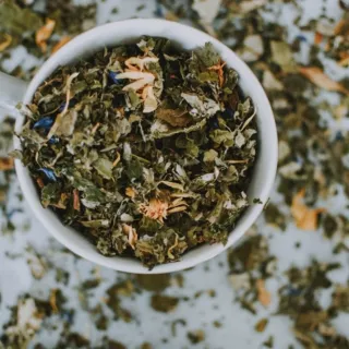 Cup filled with dried herbal tea leaves on a white surface.