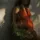Pregnant woman in red dress holding flowers, standing against a sunlit wall.