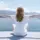 Person in white sitting by the sea with arms outstretched, mountains in the background.