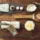 Skincare items on wooden table: brush, cloth, candle, cream, rosemary, and a white rose.