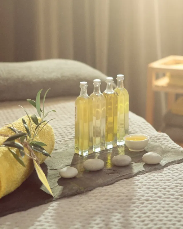 Yellow towel, olive branch, and oil bottles on a spa bed with stones and a small bowl.