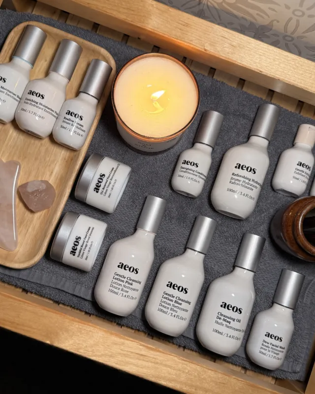 Skincare products and candle on a wooden tray with a gua sha tool and brushes.